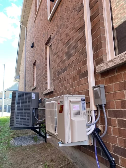 Mitsubishi heat pump outdoor unit mounted on wall brackets beside a brick home in Innisfil