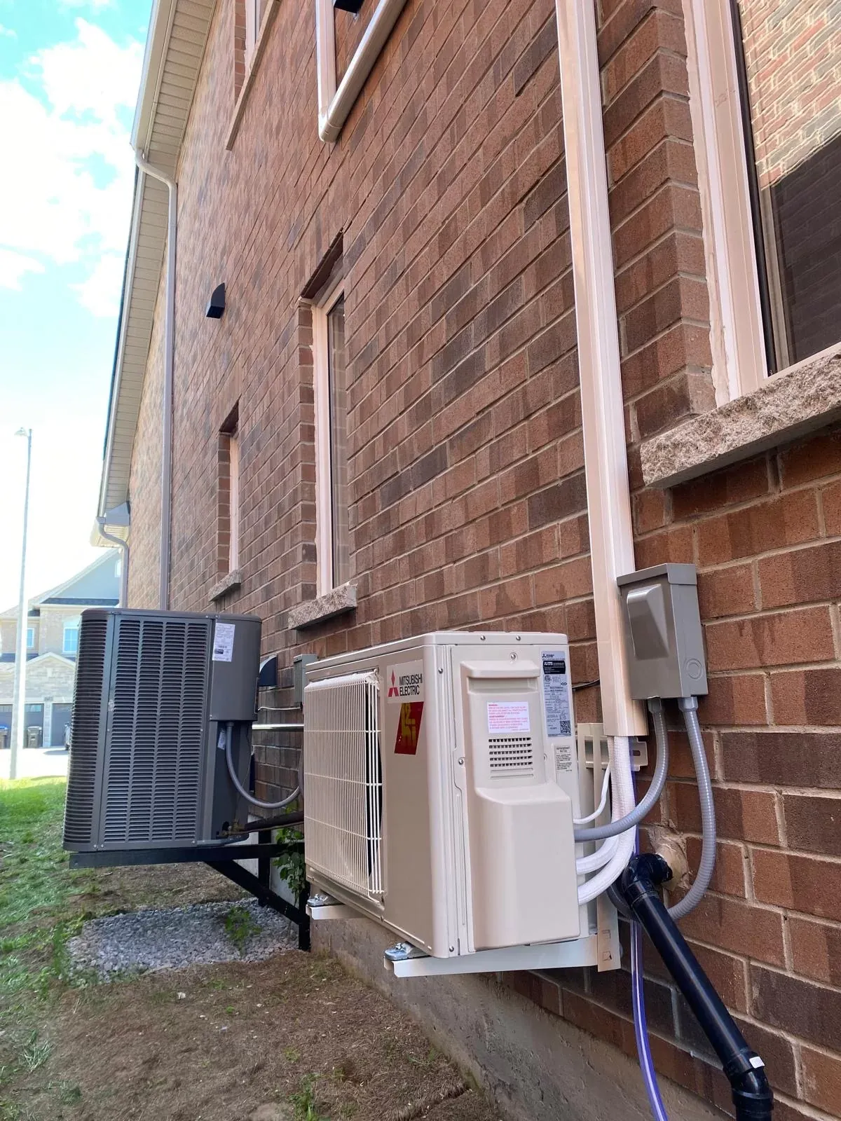 Mitsubishi heat pump outdoor unit mounted on wall brackets beside a brick home in Innisfil